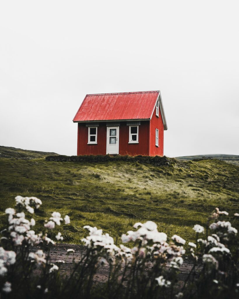 Lite rødt hus som står alene med blomster i forgrunnen